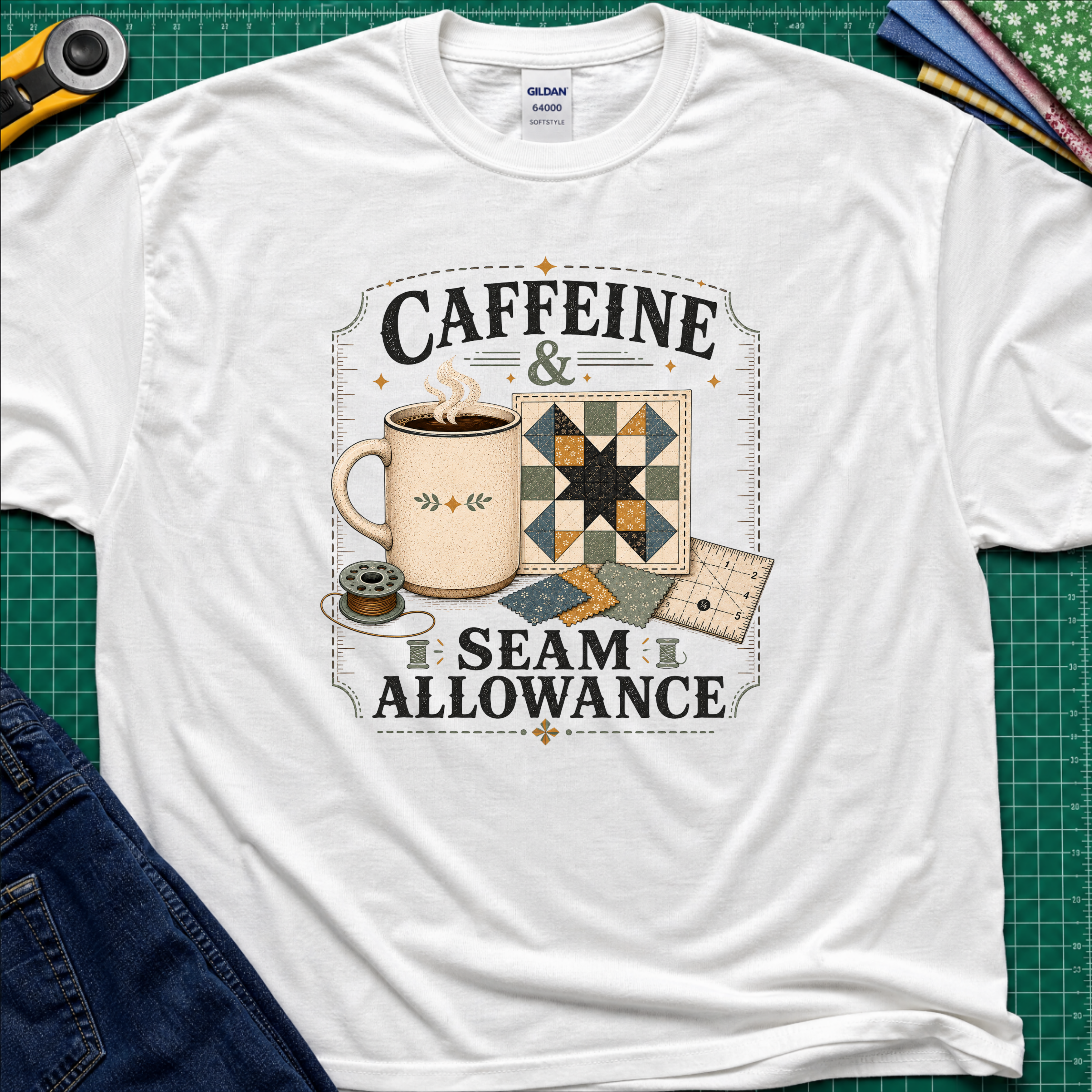 A white Gildan t-shirt laid flat on a green cutting mat background, featuring a graphic print that reads 'CAFFEINE & SEAM ALLOWANCE' around an illustration of a coffee mug, sewing thread spool, and quilt blocks.