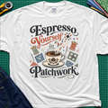 An white Gildan t-shirt with a colorful retro graphic that reads 'Espresso Yourself in Patchwork' around an illustration of a coffee cup, fabric swatches and cotton reels. It is laid flat on a green cutting mat with a rotary cutter, fabric stack and blue jeans partially visible in the corners.