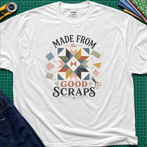 A white Gildan t-shirt with a retro-style quilted scrapbook graphic and the text 'MADE FROM the GOOD SCRAPS'. The shirt is styled in a flat-lay on a green cutting mat with sewing tools and fabric.