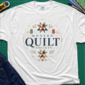 A white Gildan t-shirt with a 'Modern Quilt Society' graphic printed on the front, with quilt blocks, thread spools and small leaves. Styled in a flat-lay on a green cutting mat with sewing tools and fabric.