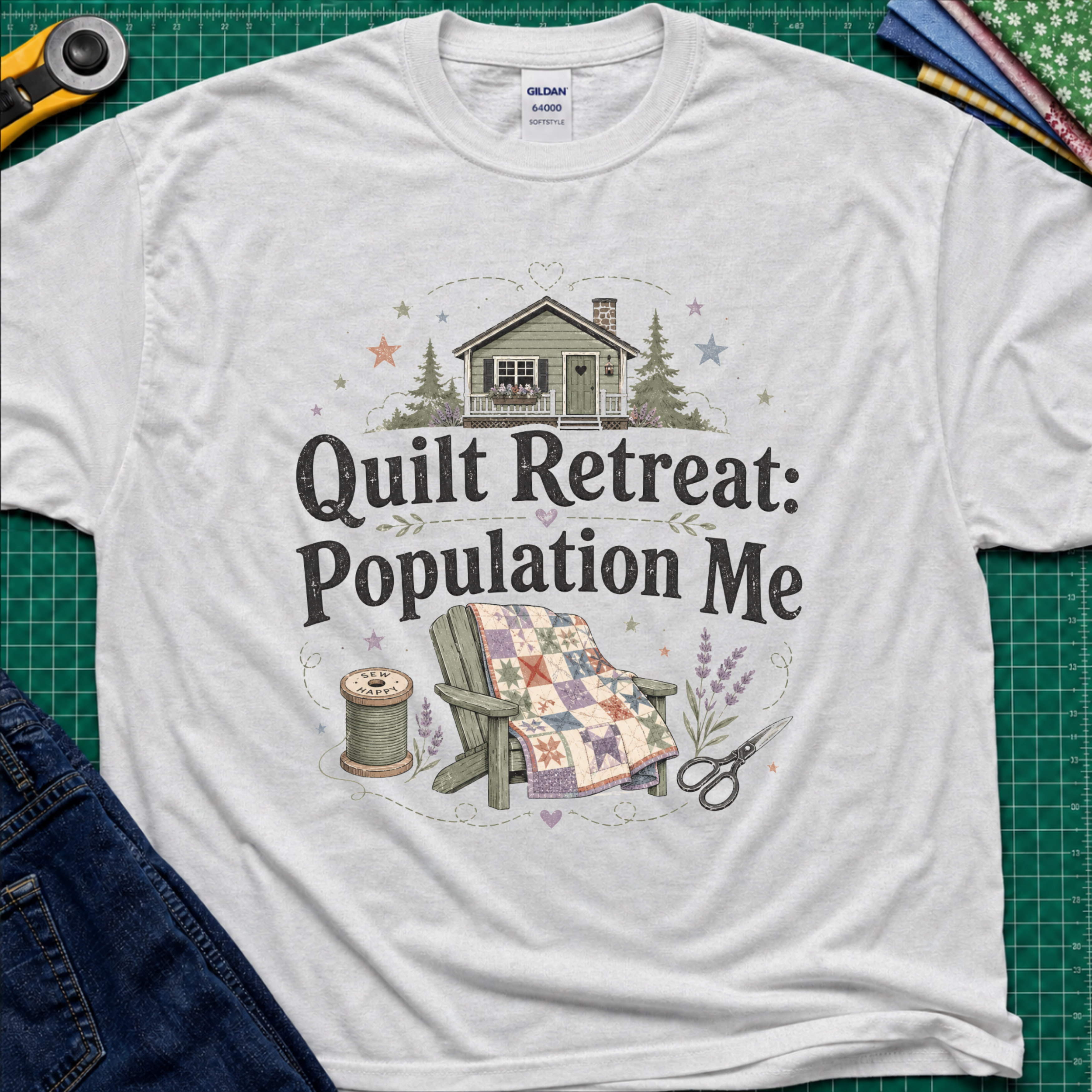 A light grey Gildan t-shirt with a 'Quilt Retreat: Population Me' graphic print, styled in a flat-lay on a green cutting mat with sewing props.