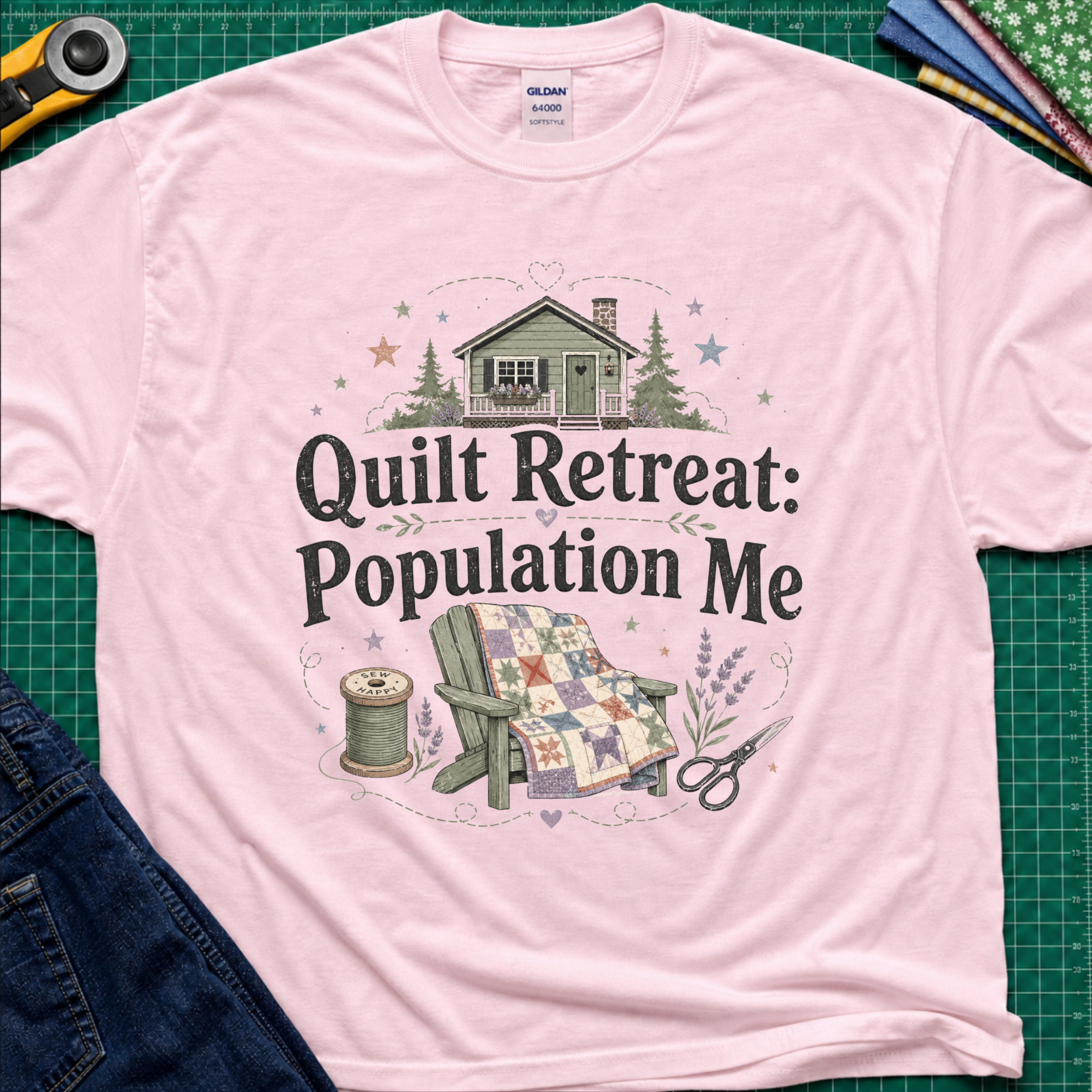 A light pink Gildan t-shirt with a 'Quilt Retreat: Population Me' graphic print, styled in a flat-lay on a green cutting mat with sewing props.