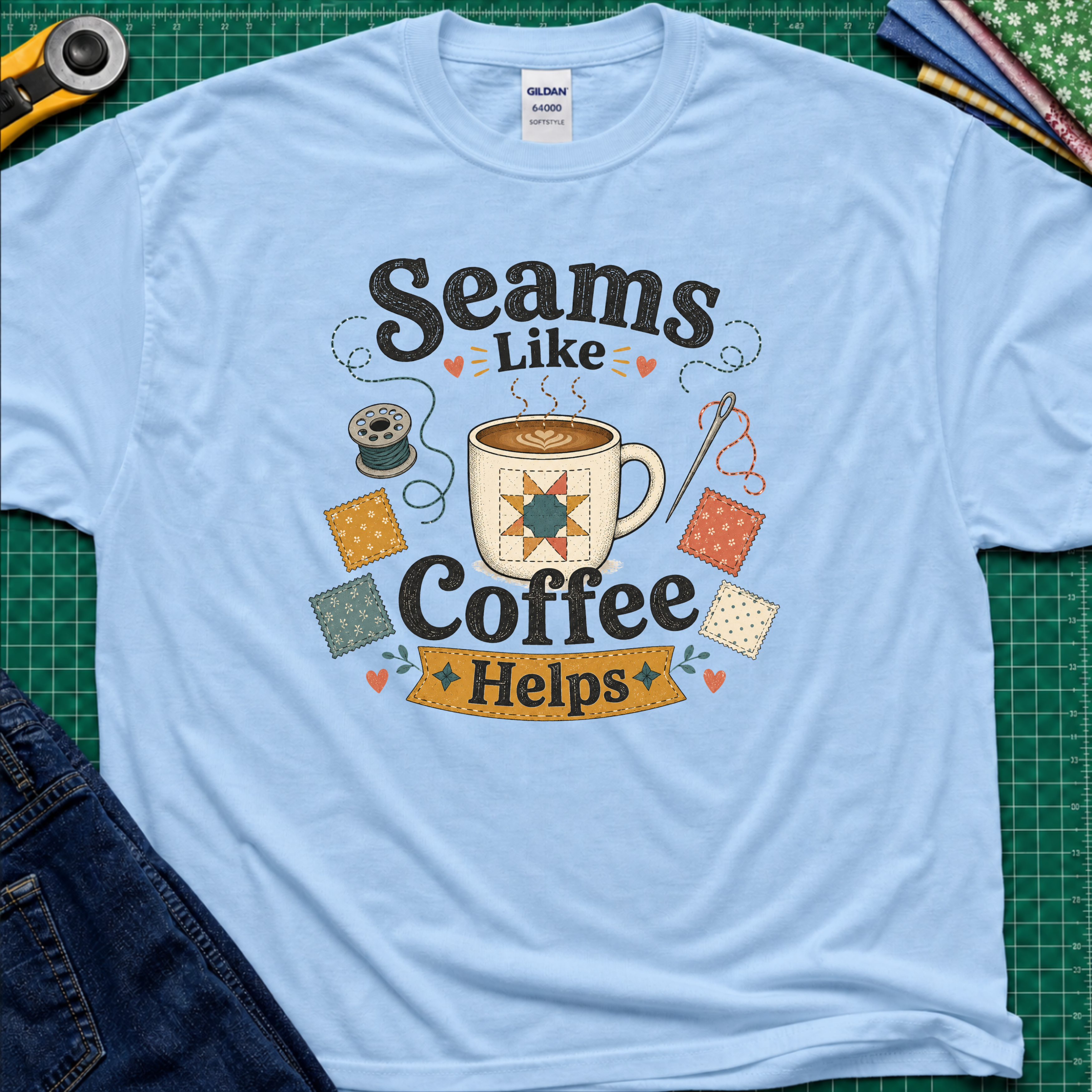 A light blue Gildan t-shirt with a colorful graphic that reads 'Seams Like Coffee Helps' with a coffee mug, fabric swatches, needle and bobbin.