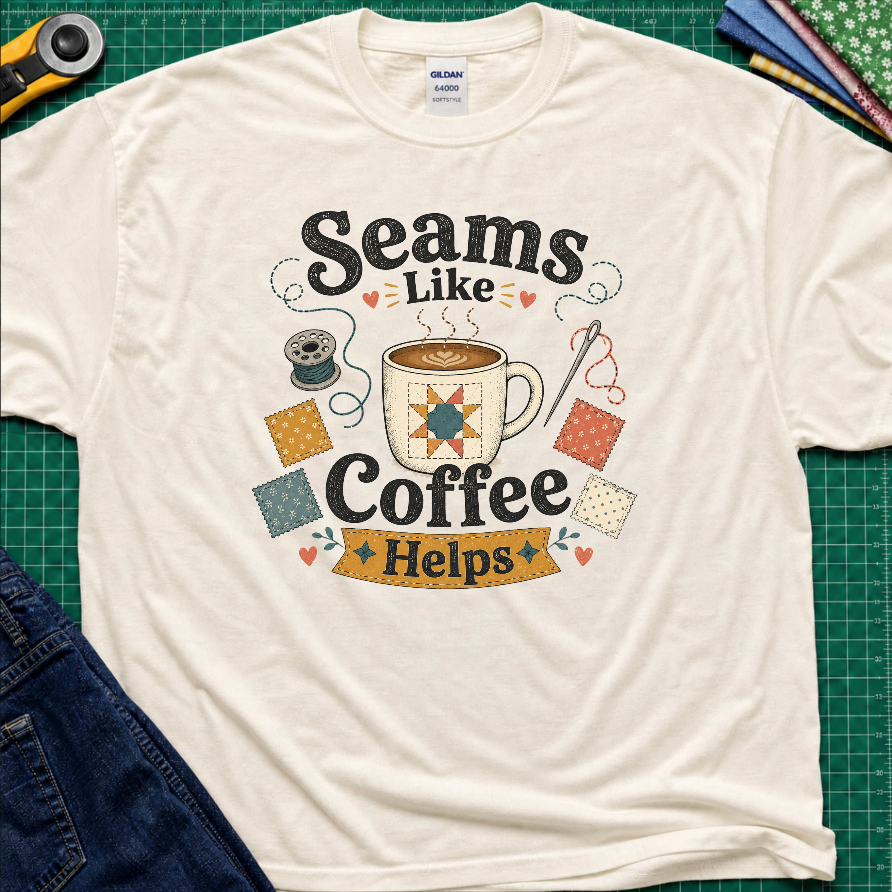 A light cream Gildan t-shirt with a colorful graphic that reads 'Seams Like Coffee Helps' with a coffee mug, fabric swatches, needle and bobbin.