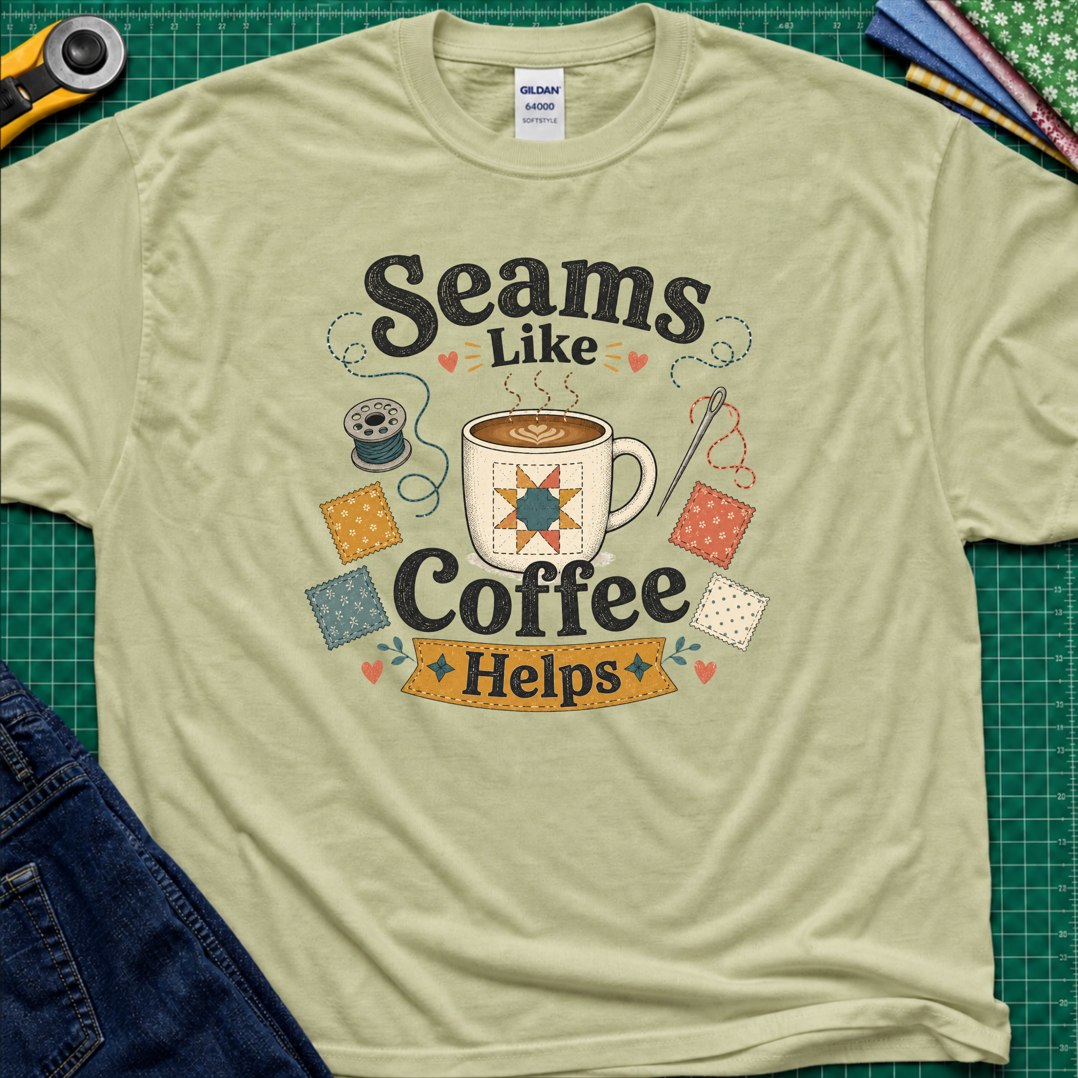 A light pistachio greenGildan t-shirt with a colorful graphic that reads 'Seams Like Coffee Helps' with a coffee mug, fabric swatches, needle and bobbin.