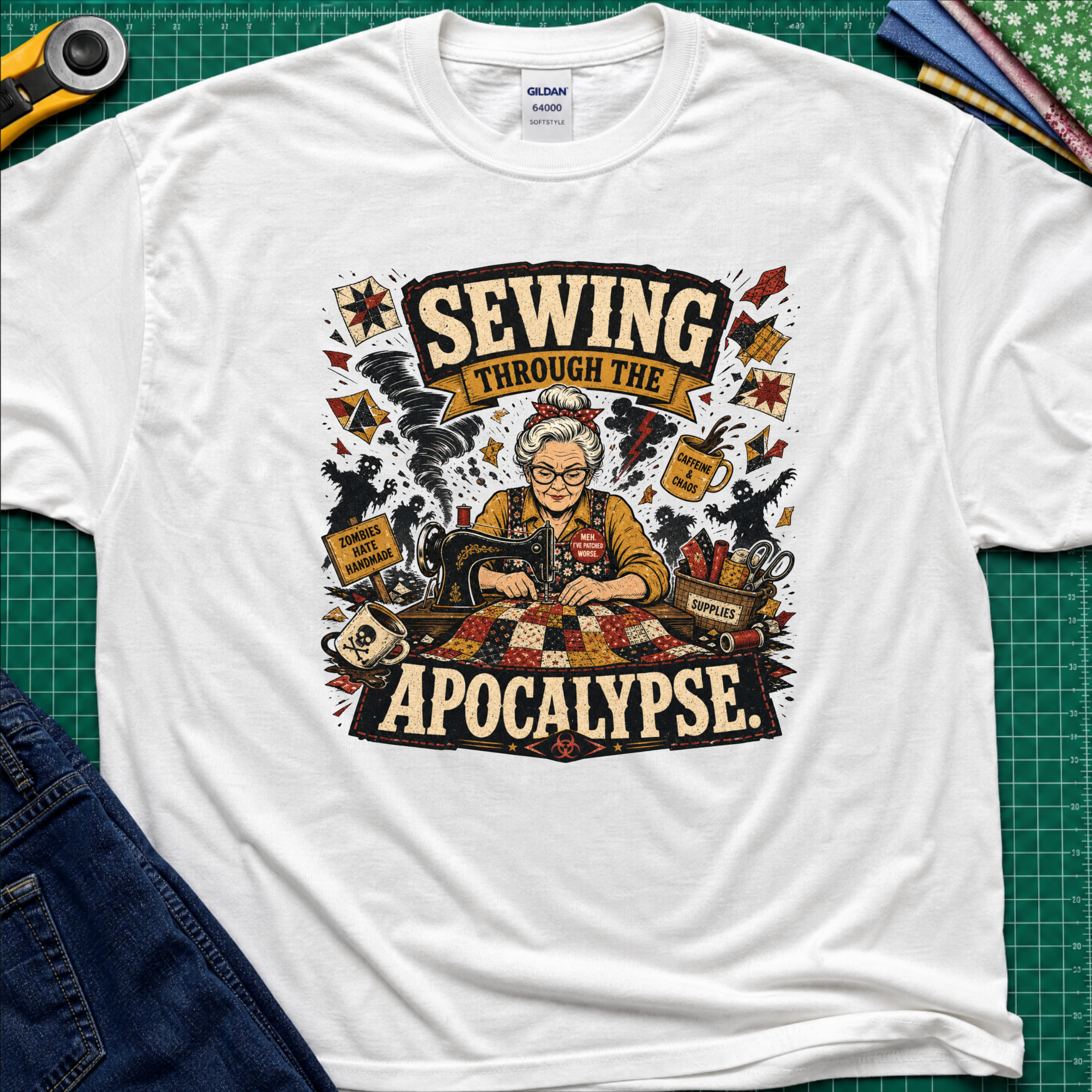 A white Gildan t-shirt laid flat on a green cutting mat, featuring a detailed graphic of a woman sewing with the text 'SEWING THROUGH THE APOCALYPSE' and various retro sewing and apocalypse-themed illustrations.
