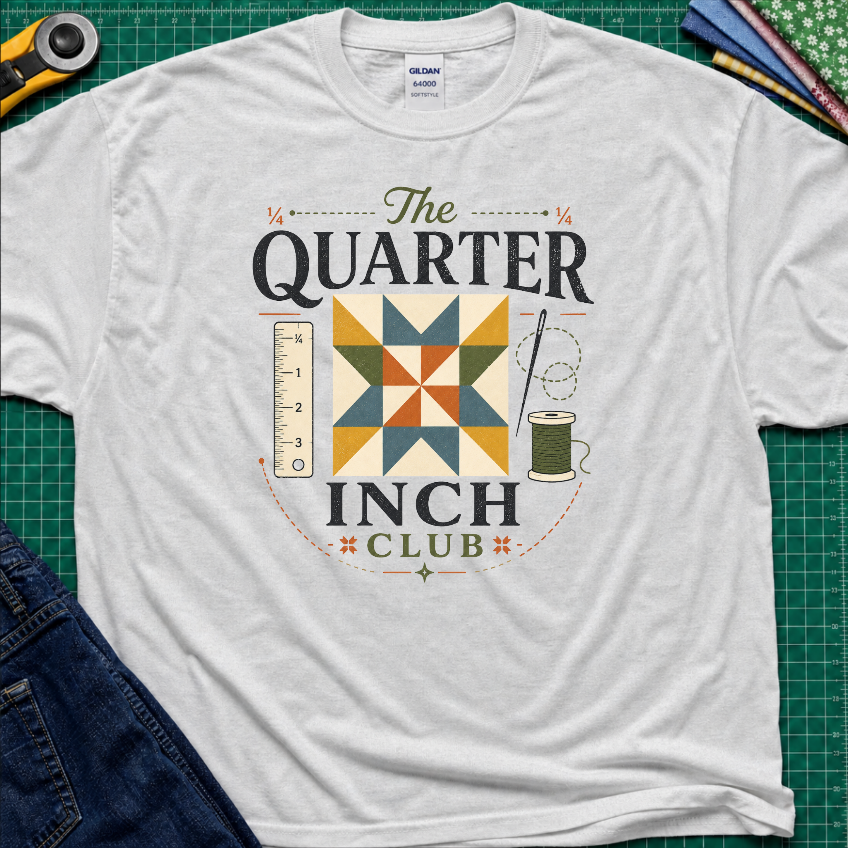 A light grey Gildan t-shirt with a retro-style quilted graphic that reads 'The QUARTER INCH CLUB'. The graphic features a geometric quilt pattern in yellow, orange, and blue, alongside a sewing ruler, spool, and needle.