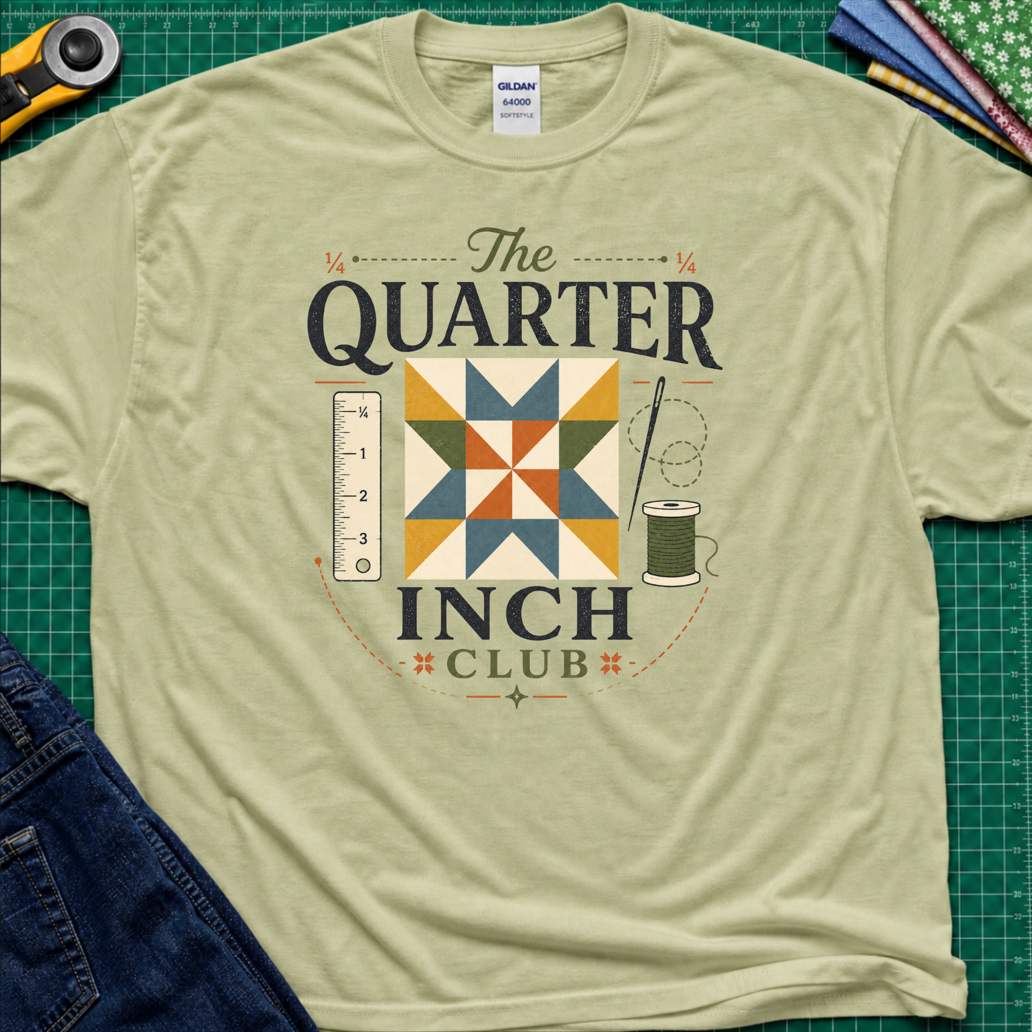 A light pistachio green Gildan t-shirt with a retro-style quilted graphic that reads 'The QUARTER INCH CLUB'. The graphic features a geometric quilt pattern in yellow, orange, and blue, alongside a sewing ruler, spool, and needle.